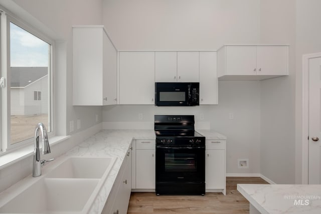 kitchen featuring light stone countertops, sink, black appliances, light hardwood / wood-style floors, and white cabinetry