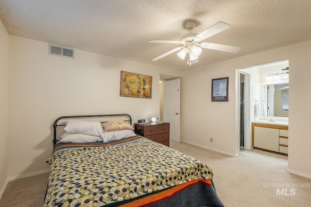 bedroom with ceiling fan, light colored carpet, a textured ceiling, and ensuite bath