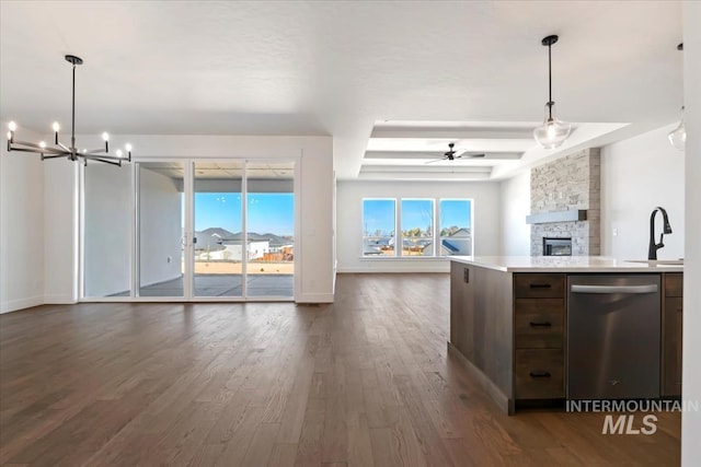 kitchen with light countertops, a sink, open floor plan, dishwasher, and a stone fireplace