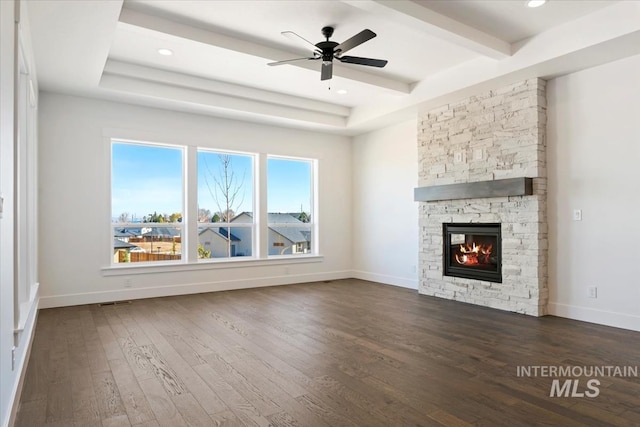 unfurnished living room with a ceiling fan, beamed ceiling, a fireplace, baseboards, and dark wood-style flooring