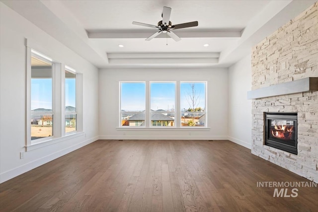 unfurnished living room with dark wood-style floors, a tray ceiling, a ceiling fan, baseboards, and a fireplace