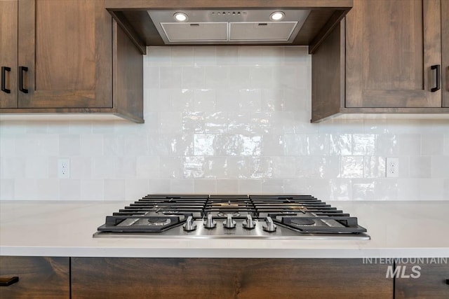 room details featuring dark brown cabinetry, light countertops, stainless steel gas stovetop, and exhaust hood