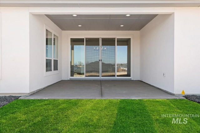 doorway to property featuring stucco siding, a yard, and a patio
