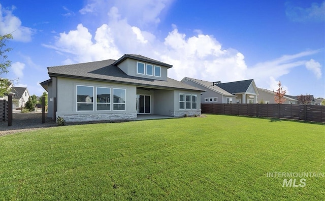 back of property with stucco siding, stone siding, fence, and a yard