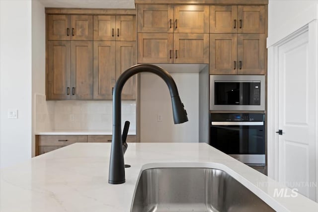 room details featuring stainless steel appliances, brown cabinetry, light stone counters, and tasteful backsplash