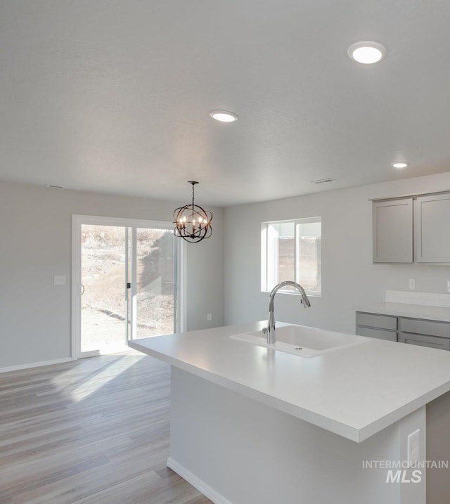 kitchen with sink, an inviting chandelier, a healthy amount of sunlight, and an island with sink