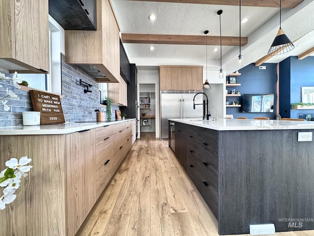 kitchen with modern cabinets, light countertops, light wood-style floors, backsplash, and a large island with sink