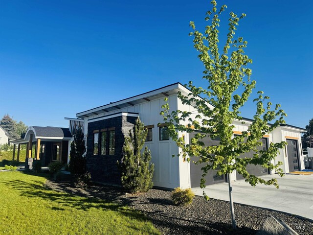 view of side of property with concrete driveway, a garage, board and batten siding, and a lawn