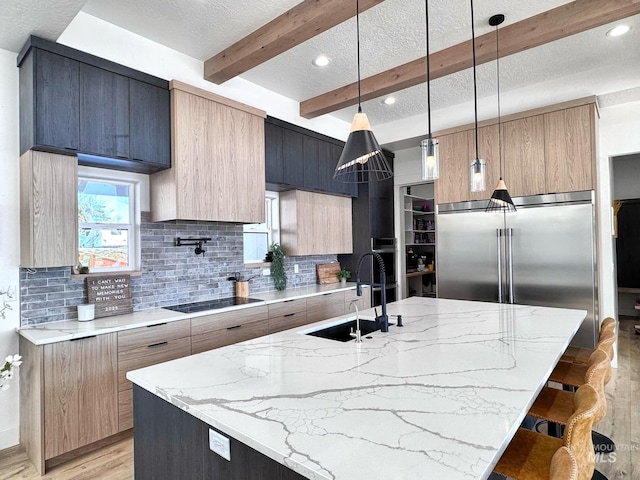 kitchen with a sink, modern cabinets, stainless steel built in fridge, decorative backsplash, and a textured ceiling