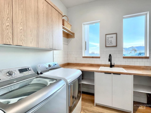 laundry area featuring washer and clothes dryer, cabinet space, healthy amount of natural light, and light wood-type flooring