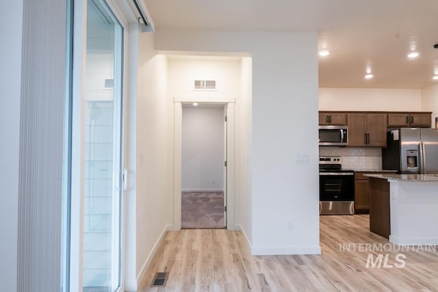 kitchen featuring dark brown cabinetry, light stone countertops, stainless steel appliances, tasteful backsplash, and light wood-type flooring