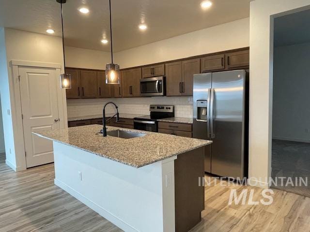 kitchen with sink, light stone countertops, stainless steel appliances, and an island with sink