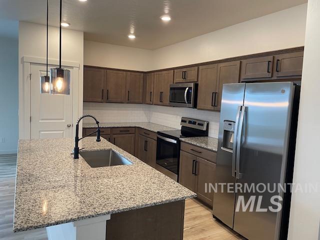 kitchen featuring pendant lighting, light stone countertops, sink, and appliances with stainless steel finishes