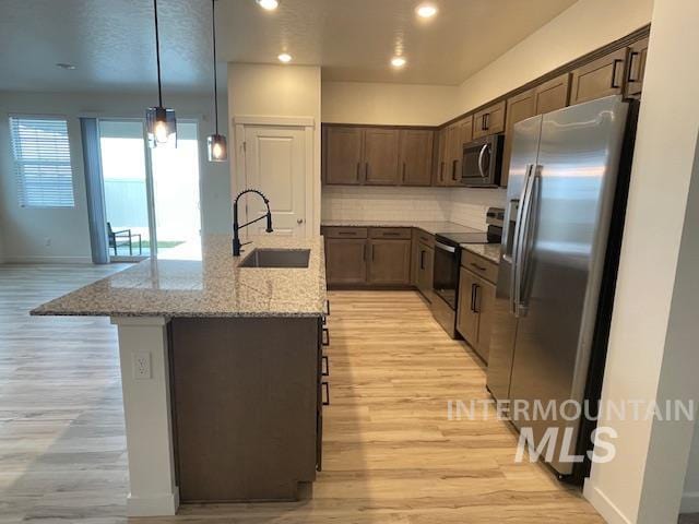 kitchen with light stone countertops, appliances with stainless steel finishes, decorative backsplash, sink, and pendant lighting