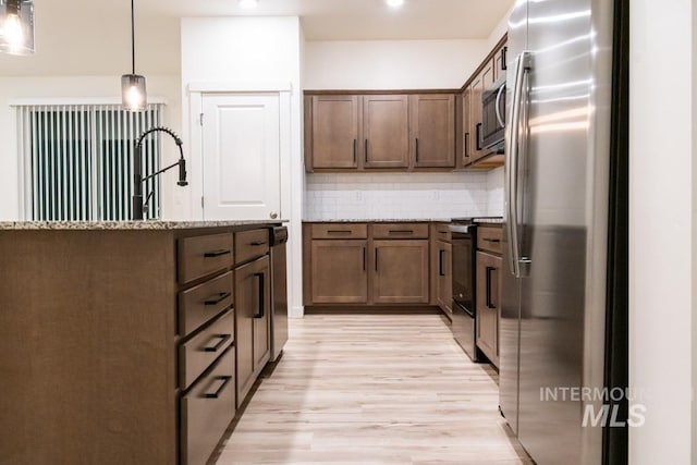 kitchen featuring decorative backsplash, light wood-type flooring, light stone counters, stainless steel appliances, and pendant lighting