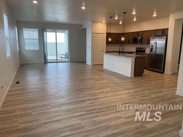 kitchen with a center island with sink, sink, appliances with stainless steel finishes, decorative light fixtures, and light hardwood / wood-style floors