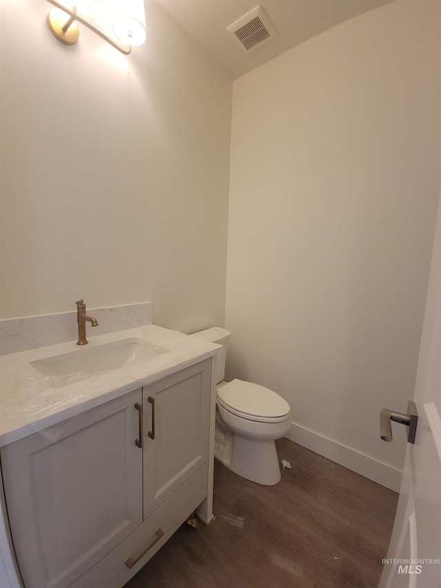 half bath with vanity, toilet, visible vents, baseboards, and wood finished floors