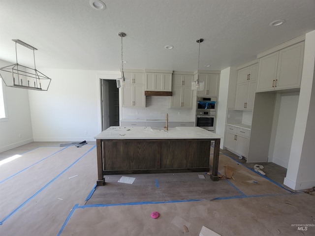 kitchen with a sink, a center island with sink, stainless steel double oven, and baseboards