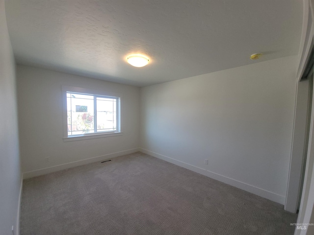 empty room featuring a textured ceiling, light carpet, and baseboards