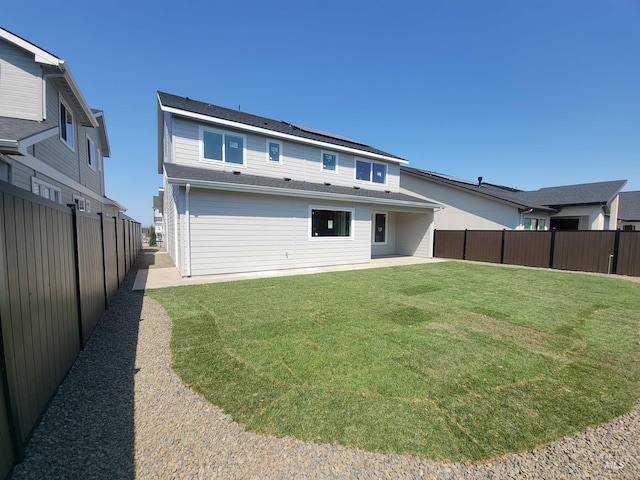 back of house featuring a lawn, roof with shingles, a fenced backyard, and a patio area