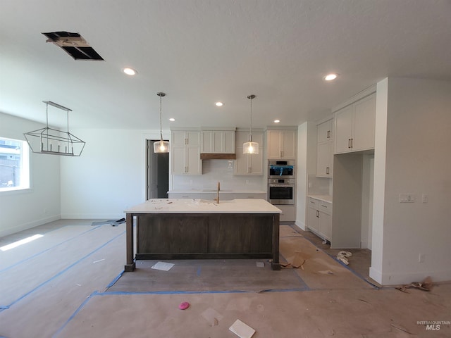kitchen with a sink, a center island with sink, baseboards, double oven, and white cabinets