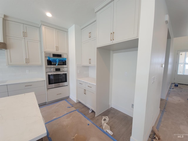 kitchen featuring white cabinetry, light stone countertops, decorative backsplash, and double oven