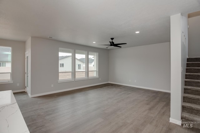 unfurnished living room featuring light wood-type flooring, ceiling fan, baseboards, and stairs