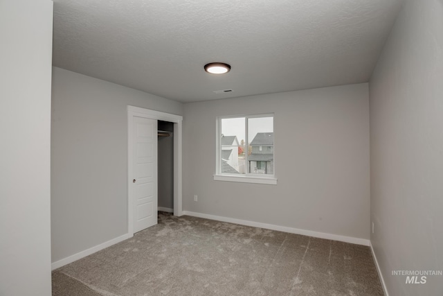 unfurnished bedroom with a textured ceiling, light carpet, visible vents, baseboards, and a closet