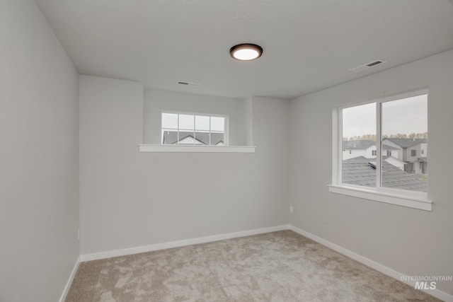 unfurnished room featuring a healthy amount of sunlight, visible vents, and light colored carpet