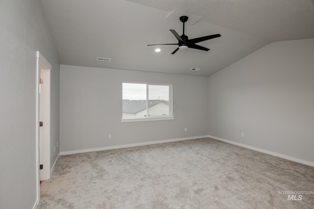 spare room featuring baseboards, visible vents, a ceiling fan, light colored carpet, and vaulted ceiling