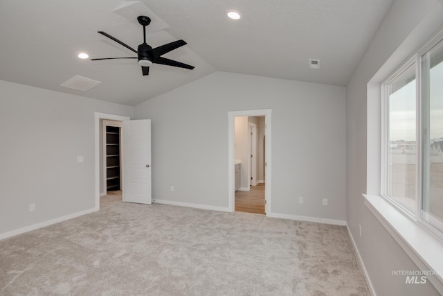 unfurnished bedroom featuring light carpet, a spacious closet, vaulted ceiling, and baseboards