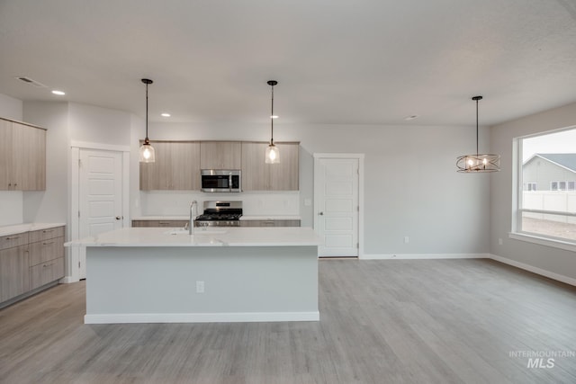 kitchen with light brown cabinets, stainless steel appliances, light countertops, an island with sink, and pendant lighting