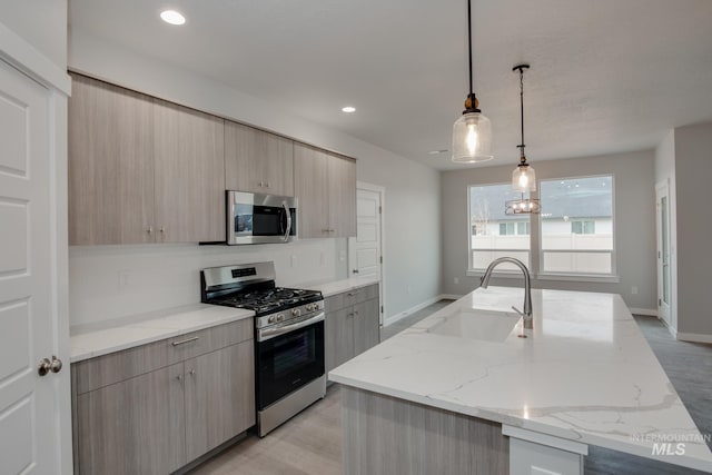 kitchen featuring stainless steel appliances, light stone counters, light brown cabinets, and a kitchen island with sink