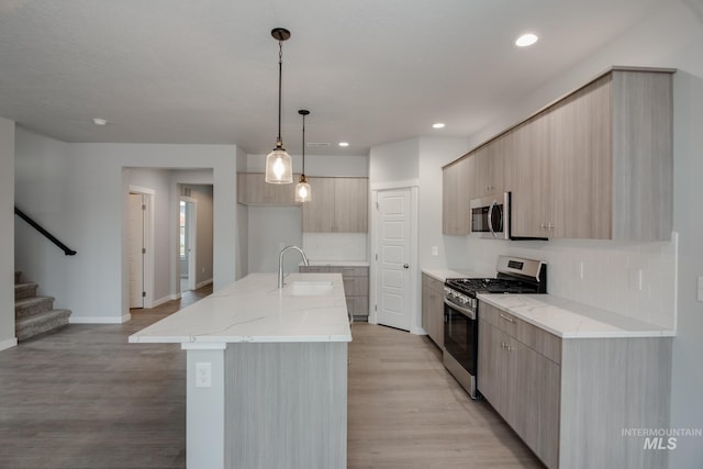 kitchen featuring pendant lighting, appliances with stainless steel finishes, a kitchen island with sink, light brown cabinets, and light stone countertops