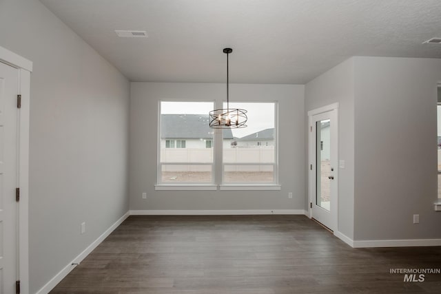 unfurnished dining area featuring baseboards, visible vents, dark wood finished floors, a textured ceiling, and a chandelier