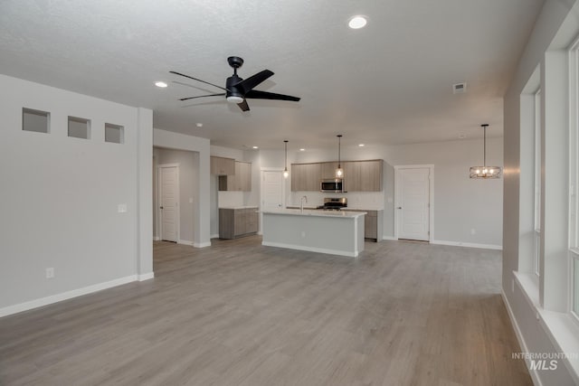 unfurnished living room featuring recessed lighting, ceiling fan with notable chandelier, visible vents, baseboards, and light wood-style floors