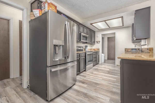 kitchen with appliances with stainless steel finishes, light wood-type flooring, and a textured ceiling