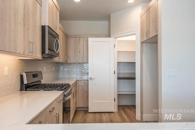 kitchen with decorative backsplash, light brown cabinets, stainless steel appliances, and light hardwood / wood-style flooring