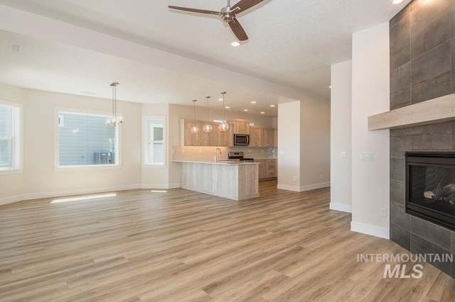 unfurnished living room featuring a tile fireplace, sink, light hardwood / wood-style floors, and ceiling fan with notable chandelier