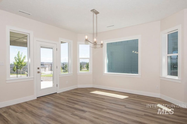 unfurnished dining area featuring a notable chandelier, plenty of natural light, and dark wood-type flooring