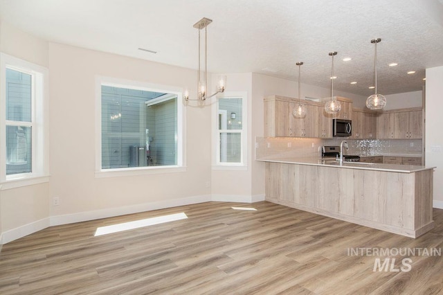 kitchen featuring kitchen peninsula, light brown cabinetry, light wood-type flooring, sink, and decorative light fixtures