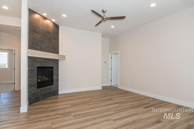 unfurnished living room with a tiled fireplace, ceiling fan, a textured ceiling, and light wood-type flooring