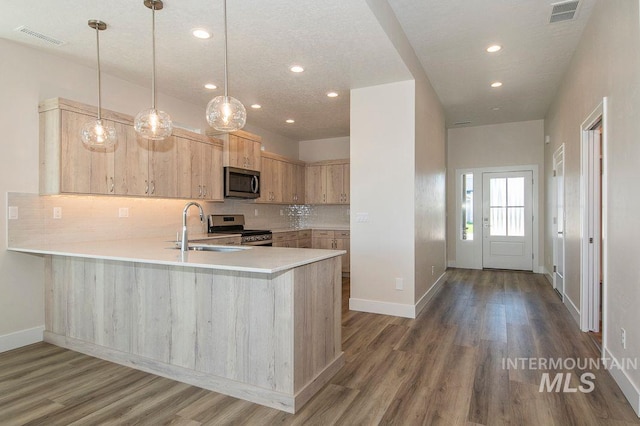 kitchen featuring backsplash, kitchen peninsula, pendant lighting, light brown cabinetry, and appliances with stainless steel finishes