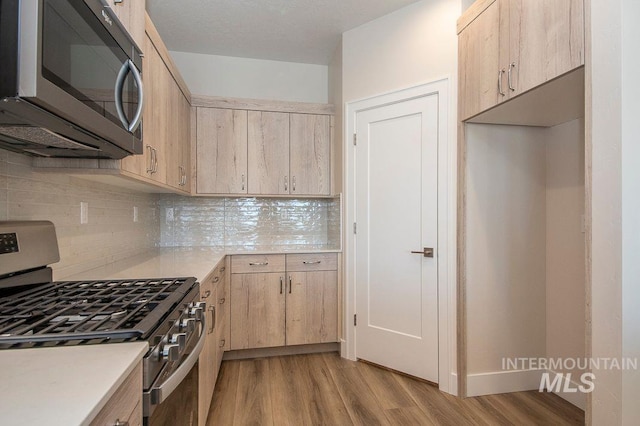 kitchen featuring light brown cabinets, stainless steel appliances, light hardwood / wood-style flooring, and tasteful backsplash