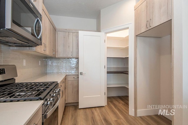 kitchen with tasteful backsplash, light brown cabinets, light hardwood / wood-style floors, and appliances with stainless steel finishes