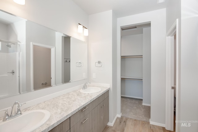 full bath featuring a spacious closet, double vanity, a sink, and wood finished floors