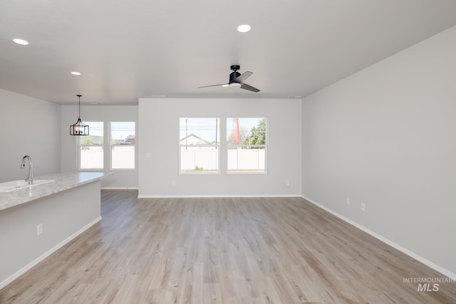 unfurnished living room featuring recessed lighting, light wood-style floors, baseboards, and a sink