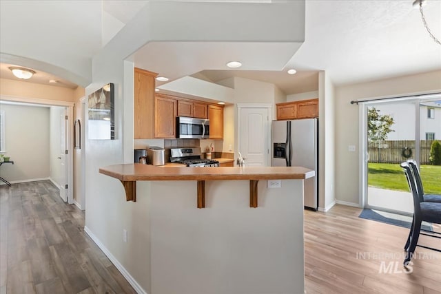 3918 Fallwood Cir, Caldwell, ID 83607 - kitchen featuring appliances with stainless steel finishes, a peninsula, light wood-style flooring, a kitchen bar, and recessed lighting