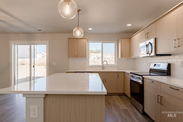 kitchen with sink, appliances with stainless steel finishes, hanging light fixtures, a kitchen island, and light brown cabinetry