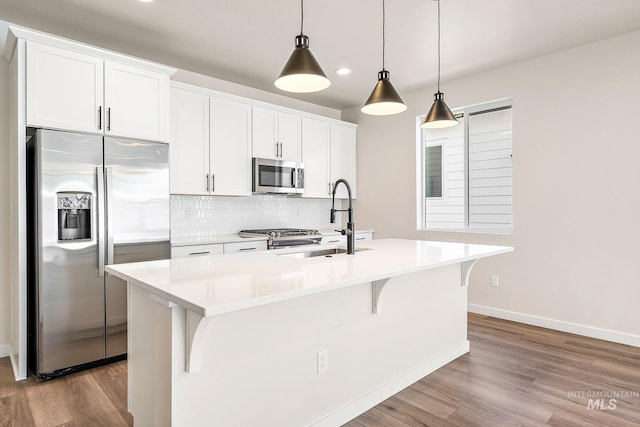 kitchen with an island with sink, stainless steel appliances, a sink, and decorative light fixtures